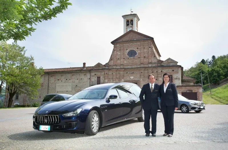 Lo staff del Centro Servizi del Funerale accanto al carro funebre, davanti a una chiesa del territorio